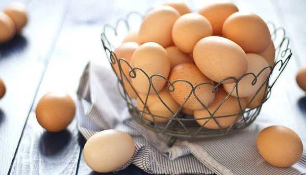 A wire basket filled with fresh brown eggs on a wooden table.