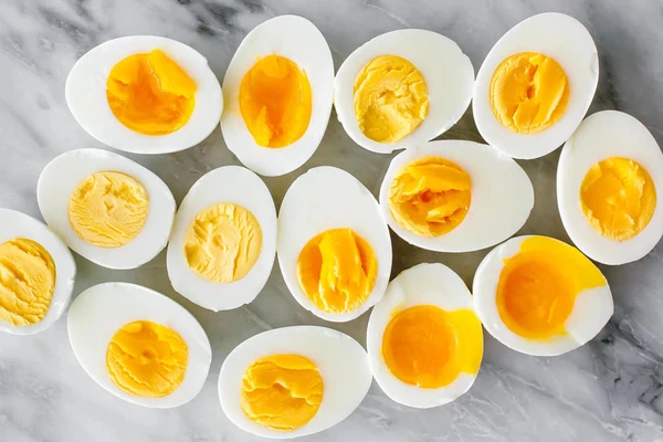 Hard-boiled egg halves on a marble surface, showcasing bright yellow yolks.