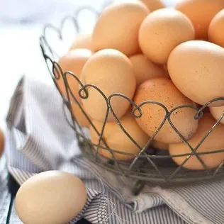 A wire basket filled with fresh brown eggs on a wooden table.